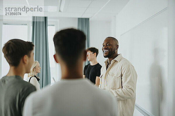 Happy male teacher discussing with students while standing by whiteboard at high school