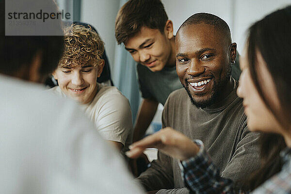 Happy male teacher looking at teenage girl discussing in classroom