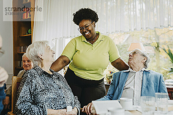 Smiling female nurse talking with elderly seniors sitting at retirement home