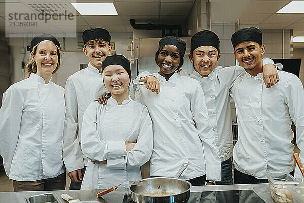 Portrait of happy male and female trainee standing with teacher at restaurant high school