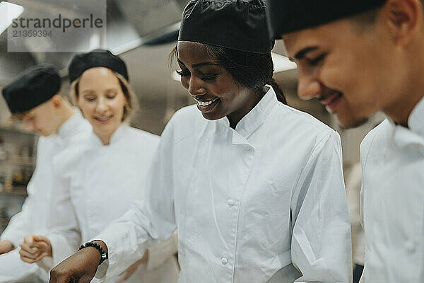 Smiling female and male trainee working by teacher in restaurant high school