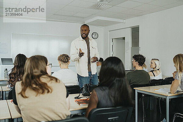 Male teacher gesturing while explaining students sitting in classroom