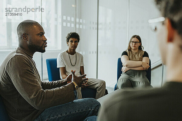 Mental health professional gesturing while guiding male and female student during group therapy at high school