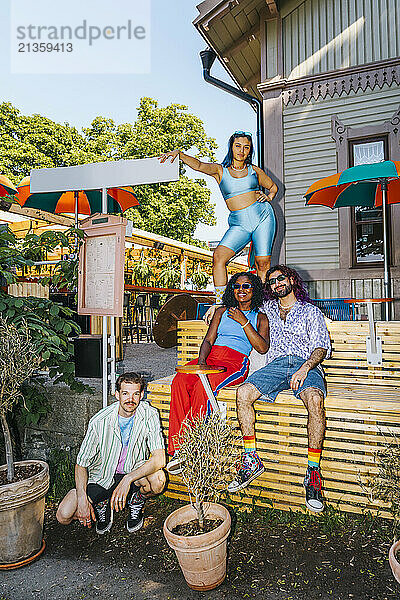 Portrait of multiracial male and female friends posing on bench outside restaurant