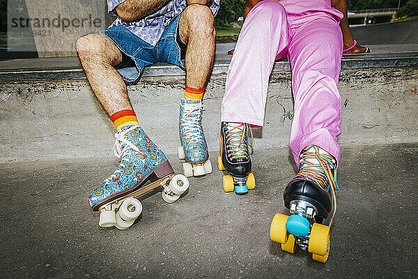 Low section of male and female friend wearing colorful roller skates while sitting near overpass