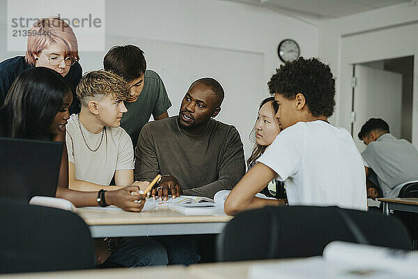 Male teacher teaching boys and girls with non-binary person in classroom