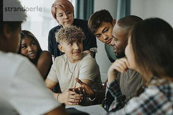 Teenage boys and girls with non-binary person listening to male teacher discussing in classroom