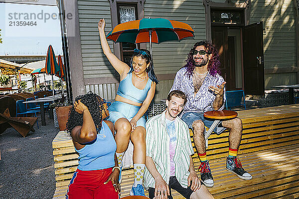 Happy male and female friends enjoying while sitting on bench outside restaurant