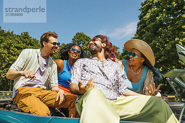 Cheerful multiracial male and female friends enjoying while sitting in car at park on sunny day