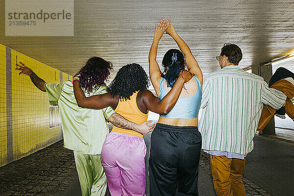 Rear view of male and female friends enjoying with each other while walking on underpass