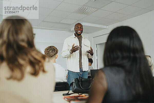 Happy male teacher gesturing while teaching high school students in classroom