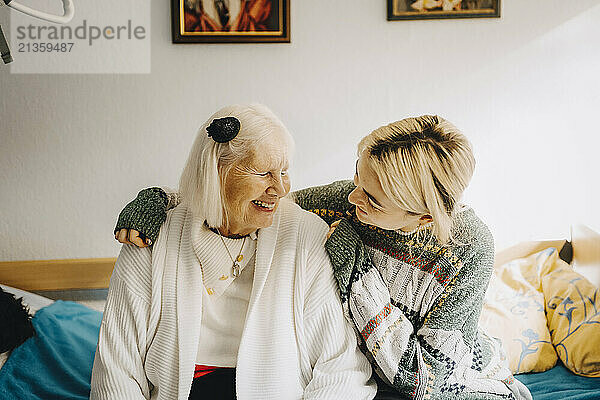 Smiling female caregiver sitting with arm around elderly woman at retirement home