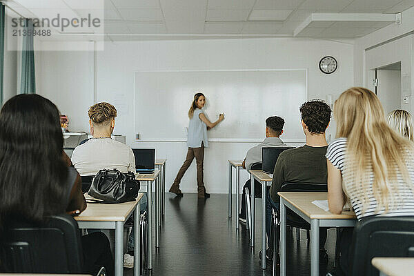 Teacher writing on whiteboard while explaining male and female students in classroom