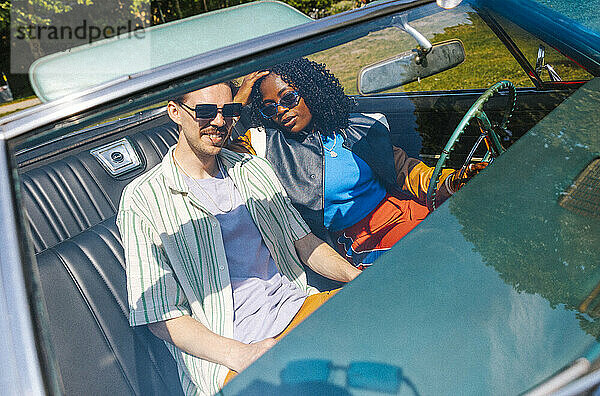 High angle portrait of male and female friends sitting in vintage car seen through windshield