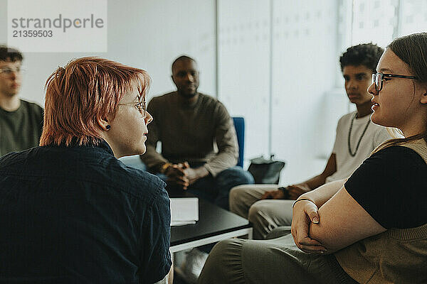 Female friend discussing with non-binary person during group therapy at high school