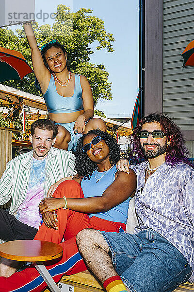 Portrait of multiracial fashionable male and female friends posing on bench outside restaurant