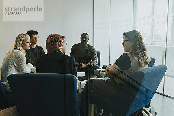 Non-binary person discussing with male and female friends during group therapy at high school