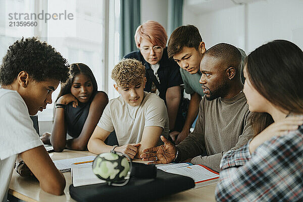 Male teacher gesturing while teaching high school students in classroom