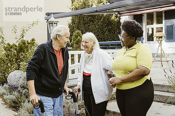 Happy senior man and woman with female caregiver near retirement home