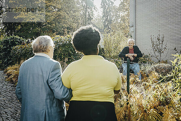 Rear view of caregiver and senior male talking with elderly man sitting in garden