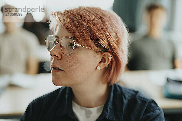 Non-binary person with pink hair wearing eyeglasses at high school