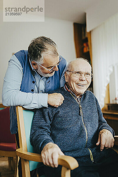 Elderly man talking with senior male friend sitting on chair at retirement home