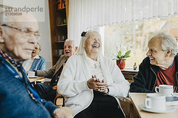 Happy male and female seniors enjoying leisure time while talking with each other at retirement home