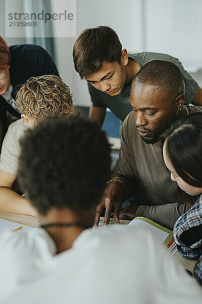 Male teacher discussing with high school students in classroom