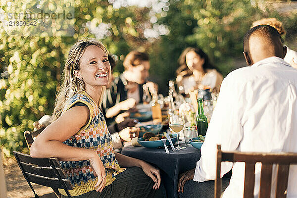 Side view portrait of smiling woman sitting on chair with friends during dinner party