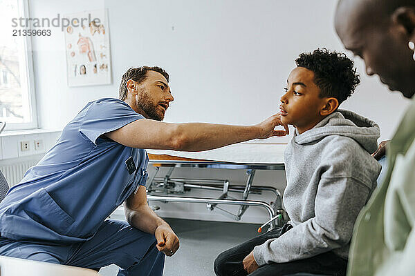 Male pediatrician checking boy's neck ache while sitting in medical examination room