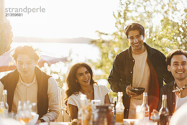 Smiling male and female friends having fun during dinner party in back yard