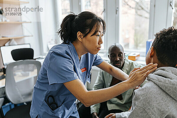 Female pediatrician checking neck ache of boy in medical examination room