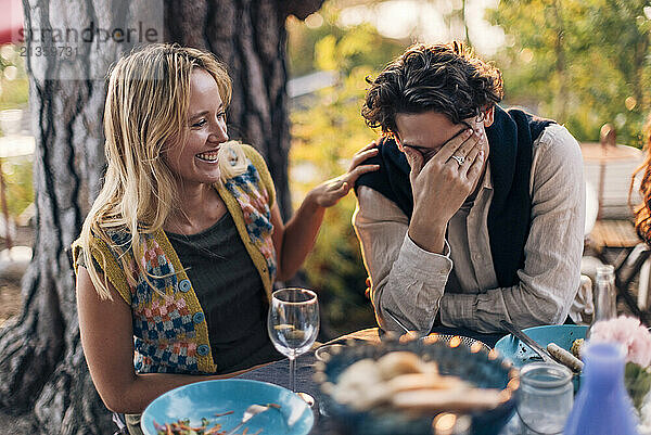 Smiling woman sitting with male friend laughing at dining table during dinner party