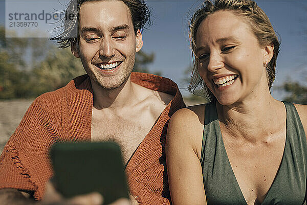 Happy male and female friends sharing smart phone at sunny day