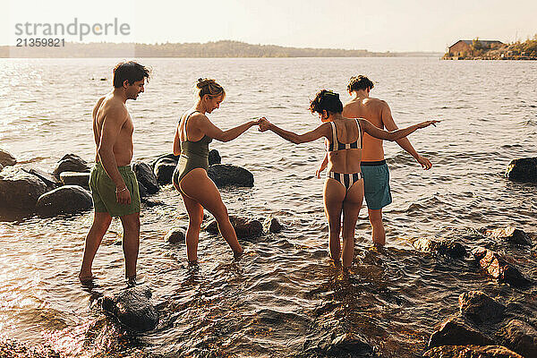 Women holding hands while walking in lake with male friends