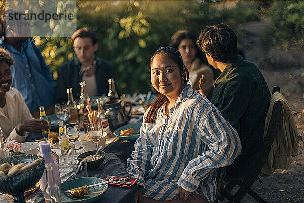 Portrait of smiling woman sitting with friends at dining table during party in back yard