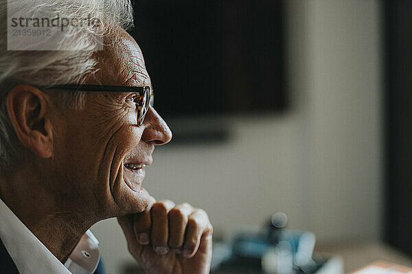 Happy senior businessman with hand on chin in office