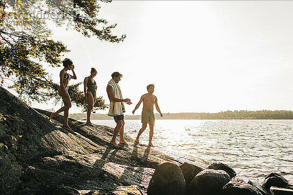 Male and female friends standing on rock near lake at sunset