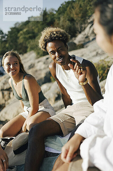 Young man gesturing while talking with female friend sitting on rock