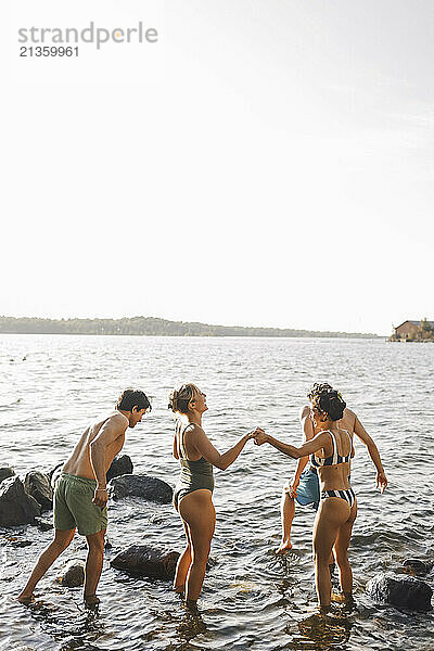 Happy male and female friends standing in lake amidst rocks