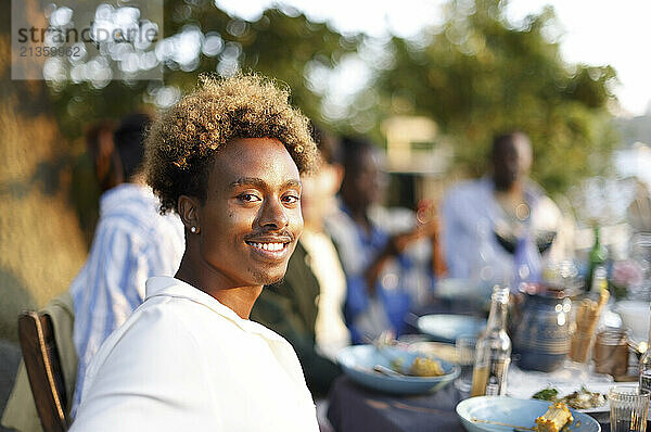 Side view portrait of smiling man with curly hair sitting at dining table during dinner party