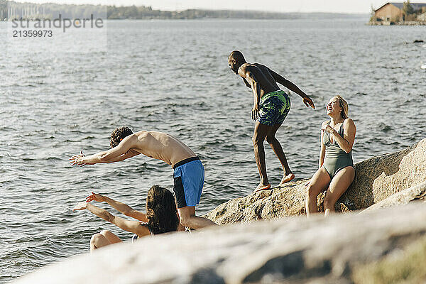 Shirtless male friends diving in lake while standing on rock during vacation