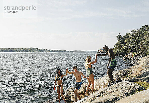 Happy male and female friends enjoying together near lake at sunny day