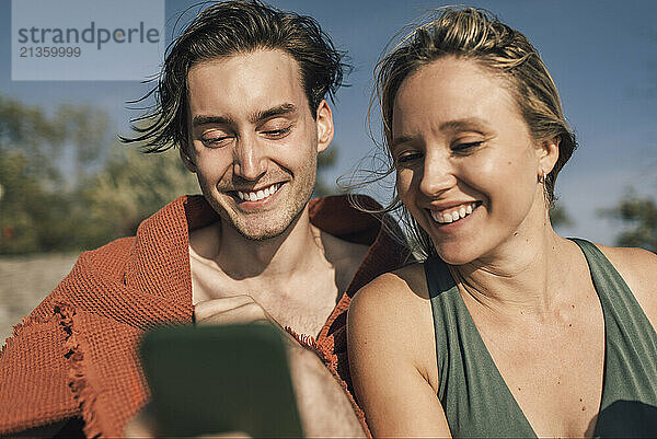 Smiling male and female friends sharing smart phone on vacation