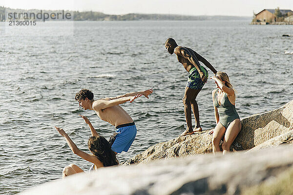 Women with shirtless male friends jumping in lake at sunny day