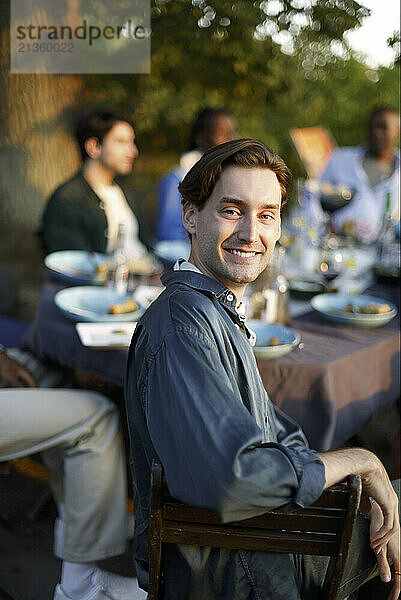 Portrait of smiling young man with friends celebrating during dinner party in back yard