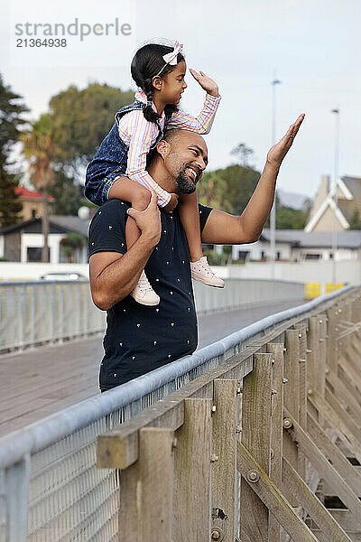 Father carrying daughter on shoulders on bridge