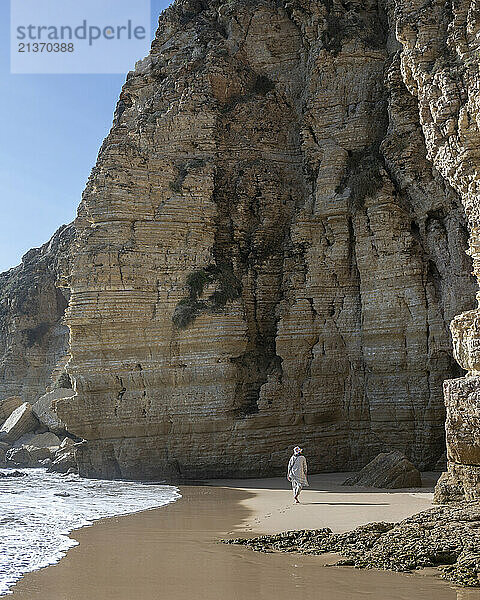 View from behind of a woman walking along the beach next to dramatic sea cliffs at the western tip of the Algarve; Sagres  Faro  Portugal