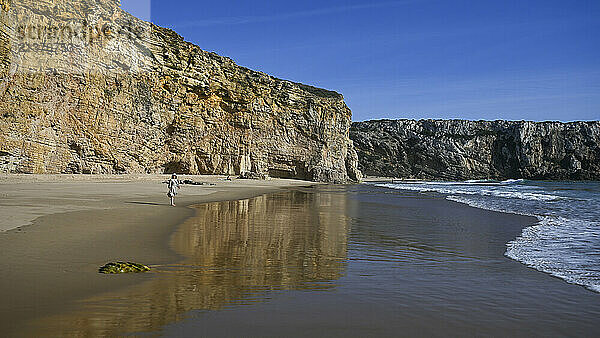 Woman stands on the beach along the rock cliffs at Sagres  which sits at the extreme western tip of the Algarve; Faro  Portugal