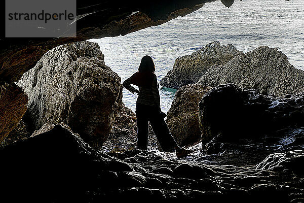 Woman stands on the rocks at low tide in the Cave of Lapa de Santa Margarida; Sao Lourenco  Setubal  Portugal